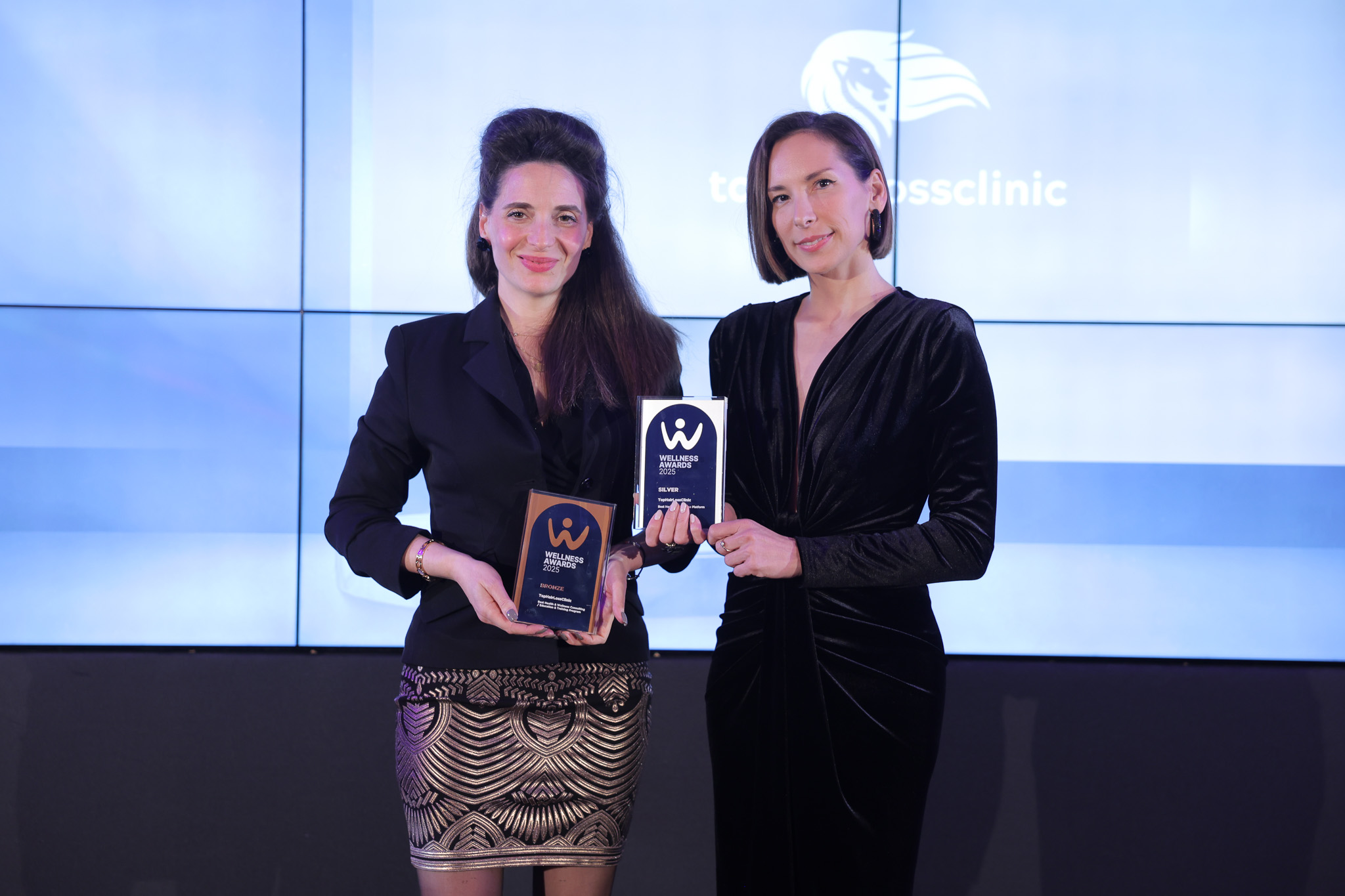 Peggy Stavrianou and Aspasia Fasoi holding two trophies at the Wellness Awards 2025